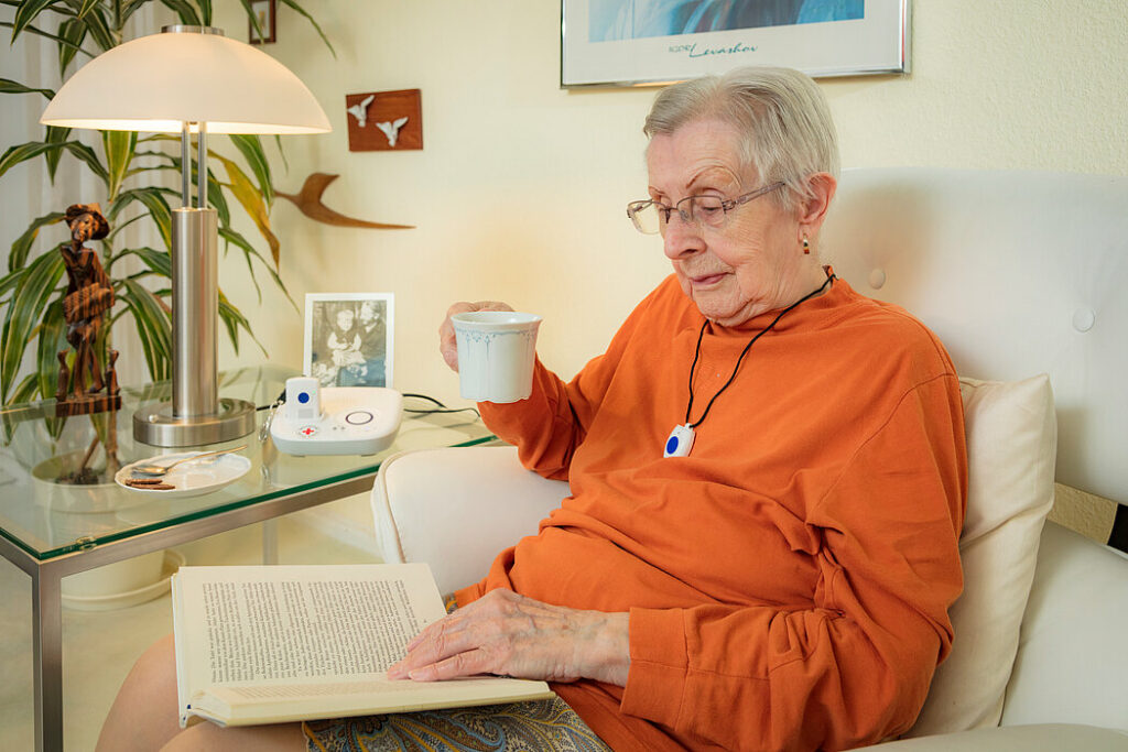 Elderly lady reading a book near a Hausnotruf device